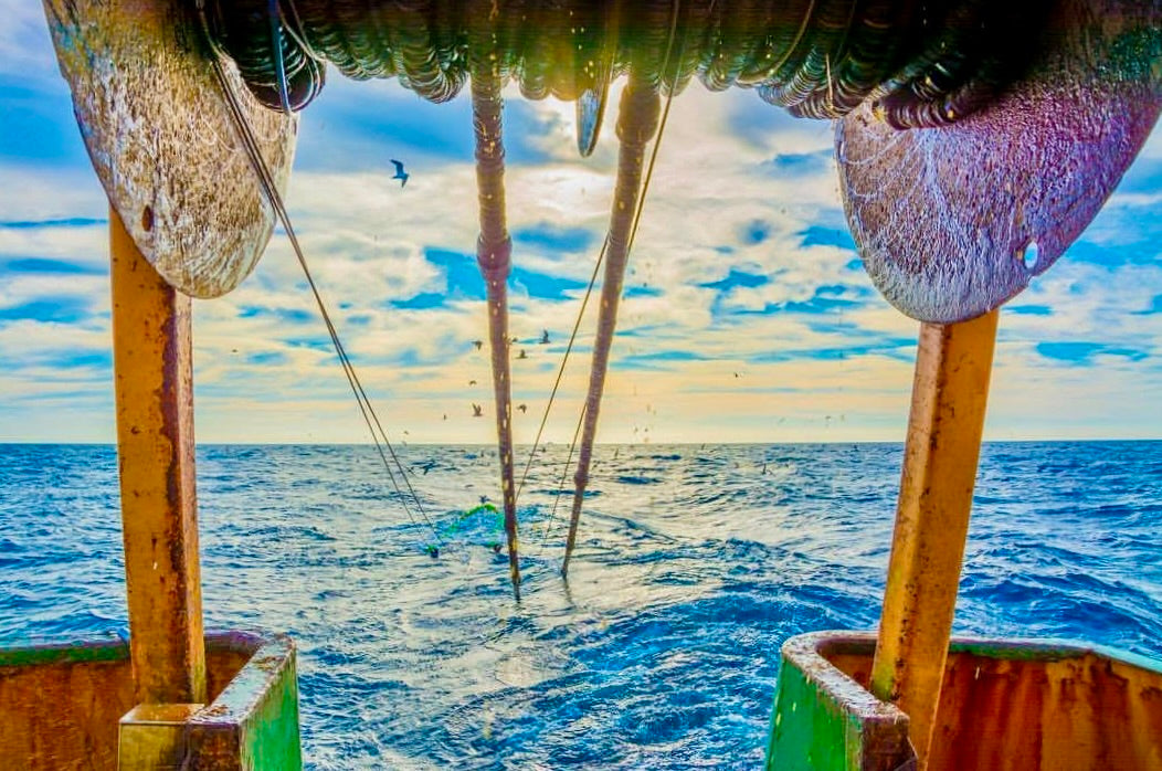 Fishing boat with nets in the water, reflecting a colorful sky.